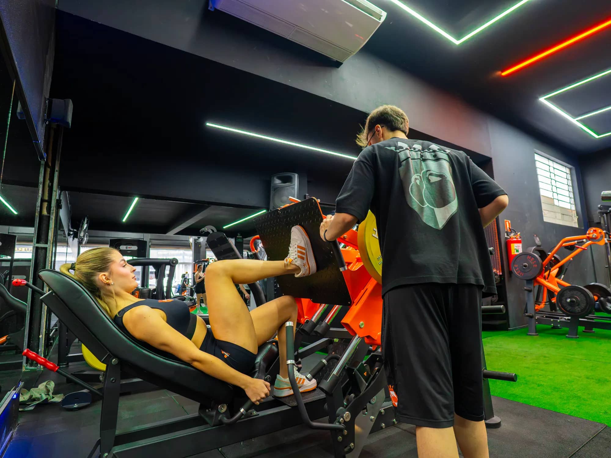 Professor acompanhando aluna no leg press